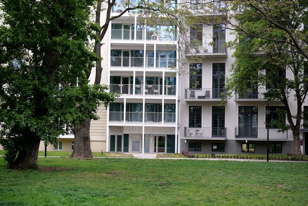 A contemporary apartment building surrounded by lush trees and open lawn area.