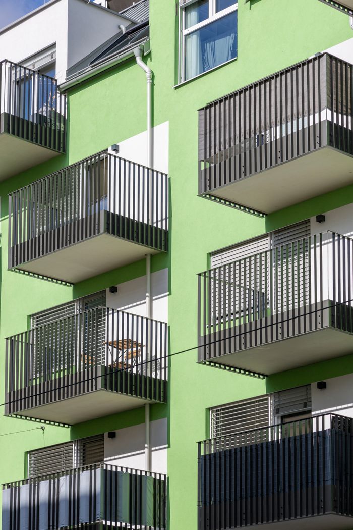 Contemporary apartment building with green facade and multiple balconies under daytime light.